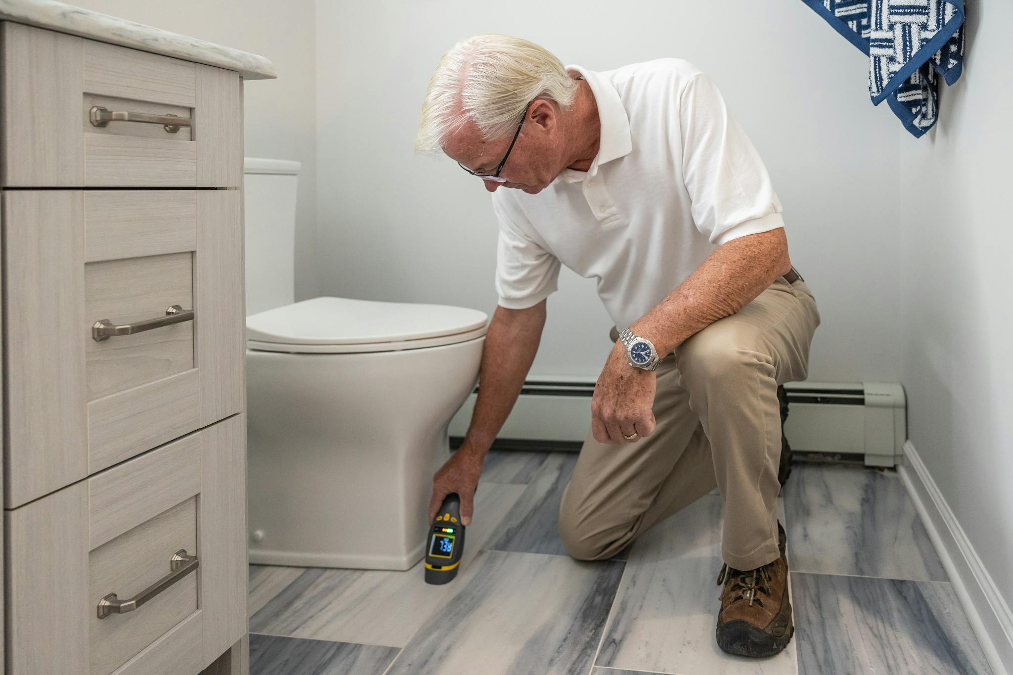A senior man using a device to inspect a bathroom for maintenance or repair.