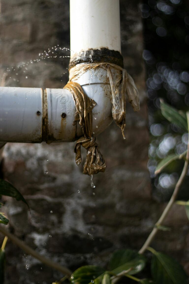 Close-up of a leaking plastic pipe outdoors with water dripping, showing wear and tear.